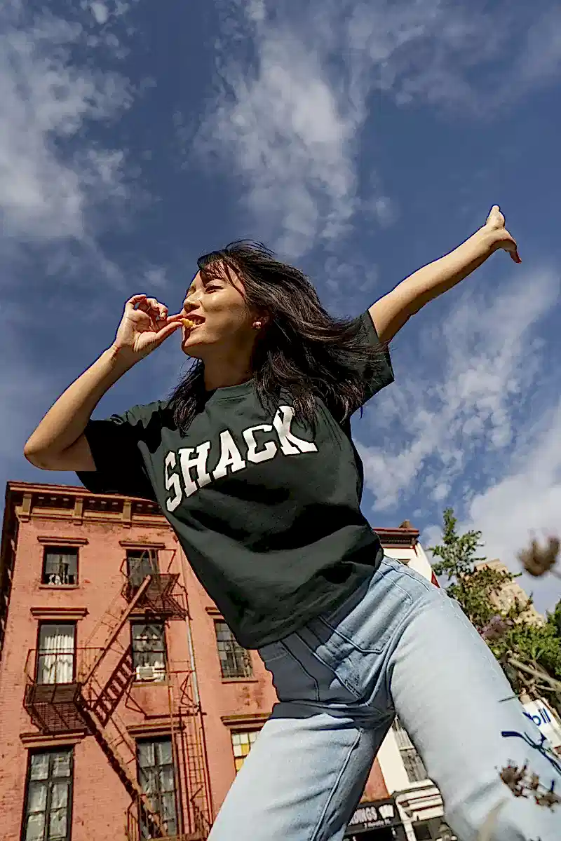 Girl outside wearing forest green Shake Shack tee and enjoying Shake Shack fries